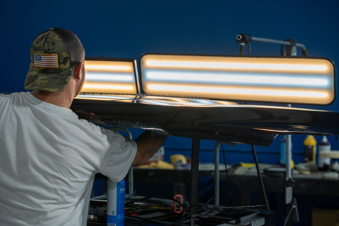 Pro PDR technician using calibrated lighting boards to map every hail dent on a vehicle hood at the Houston shop